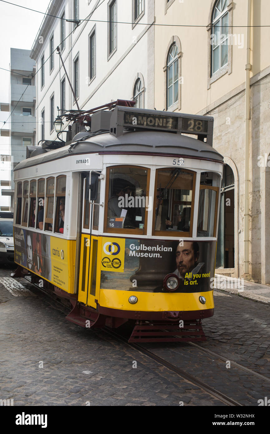 Gelbe und weiße vintage Straßenbahn auf die Straßenbahn 28 route (Wagen 552) Richtung Westen bergab auf engen, gepflasterten Straße der Stadt auf der Rua Vitor Cordon Lissabon, Portugal Stockfoto