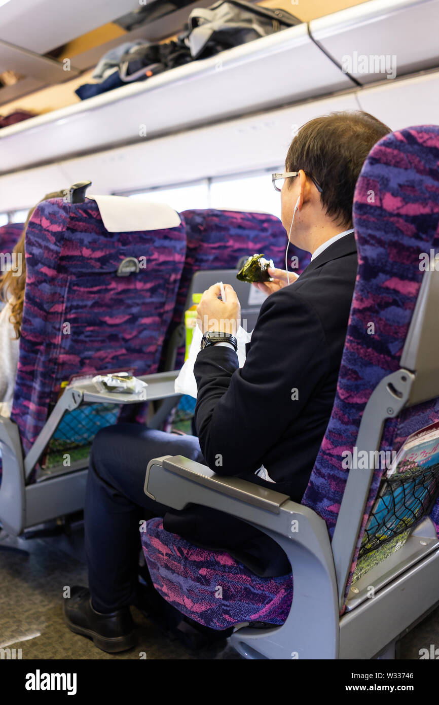 Tokyo, Japan - 4. April 2019: Unternehmer sitzen im Hochgeschwindigkeitszug Shinkansen mit Tisch, Reis essen Ball onigiri auf JR Rail Shinjuku Bahnhof s Stockfoto