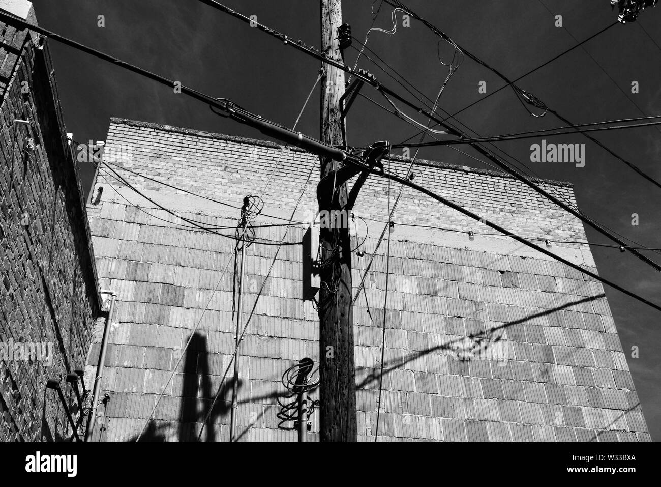 Ein Blick nach oben von mehreren elektrischen Leitungen und Telefon Kabel schneiden an einer hölzernen Mast gegen alte rote Ziegel und Beton Gebäude, USA Stockfoto