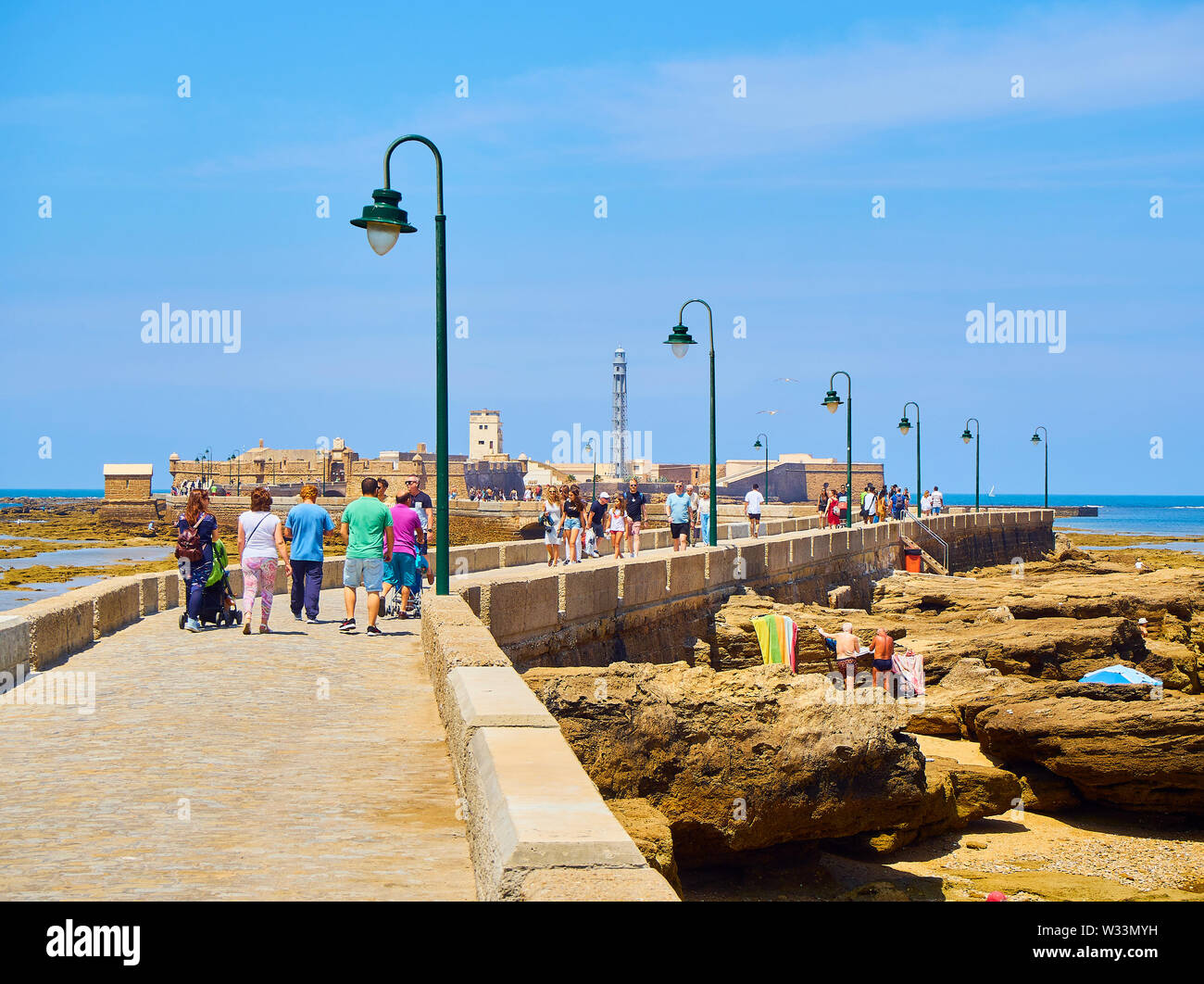 Die Menschen genießen Sie ein Sonnenbad in La Caleta Strand mit dem San Sebastian Castle, eine Festung in La Caleta Insel, im Hintergrund. Cadiz, Spanien. Stockfoto