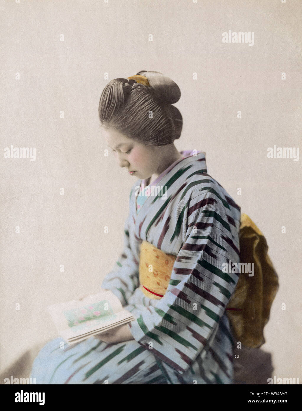 [1890s Japan - Japanische Frau im Kimono] - junge japanische Frau im Kimono und traditionelle Frisur, ein Buch zu lesen. 19 Vintage albumen Foto. Stockfoto