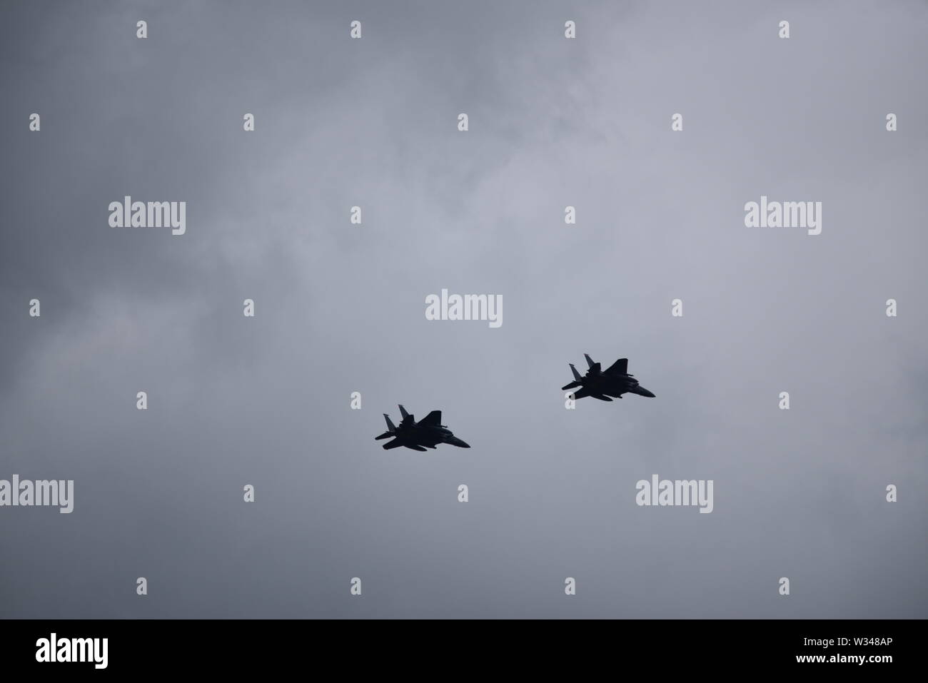 Paar F15 Eagle US-jet Kampfflugzeuge in der Ferne vor einem dunklen Grau bewölkter Himmel fliegen Stockfoto