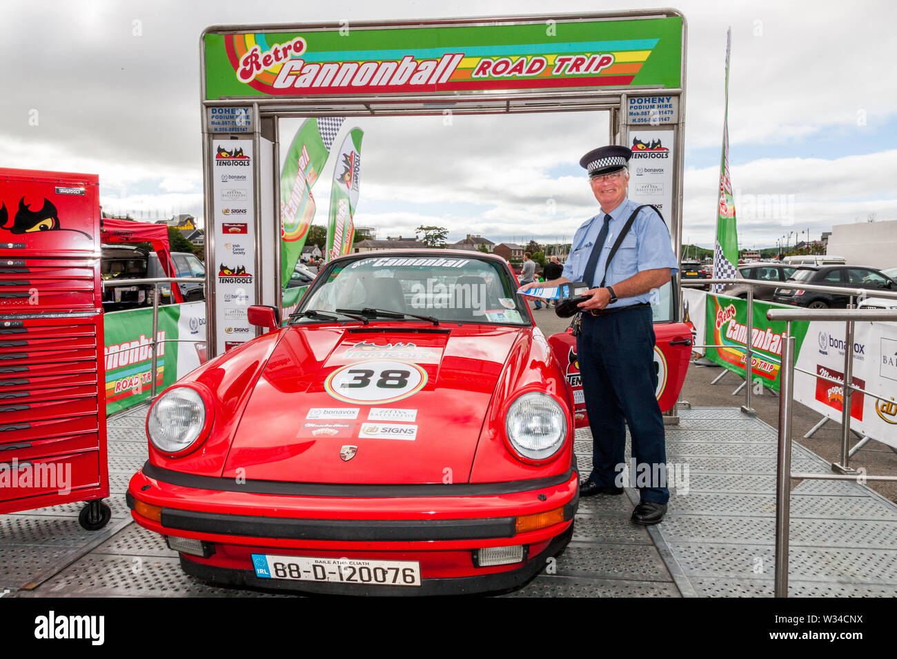 Kinsale, Cork, Irland. 12. Juli, 2019. Verkehrspolizist Tim O'Donovan Vorbereitung ein Ticket für einen Porsche auf der Startlinie der Cannononball Retro Road Trip in Kinsale, Co Cork, Irland zu geben. Die klassischen Durchlauf beginnt in Kinsale und nimmt in Healy Pass, Kenmare, Molls Gap, Zoll Strand, Dingle, Slea Head, Conor Pass, Tralee und beendet am Bunratty Castle am 13. Juli 2019. Quelle: David Creedon/Alamy leben Nachrichten Stockfoto