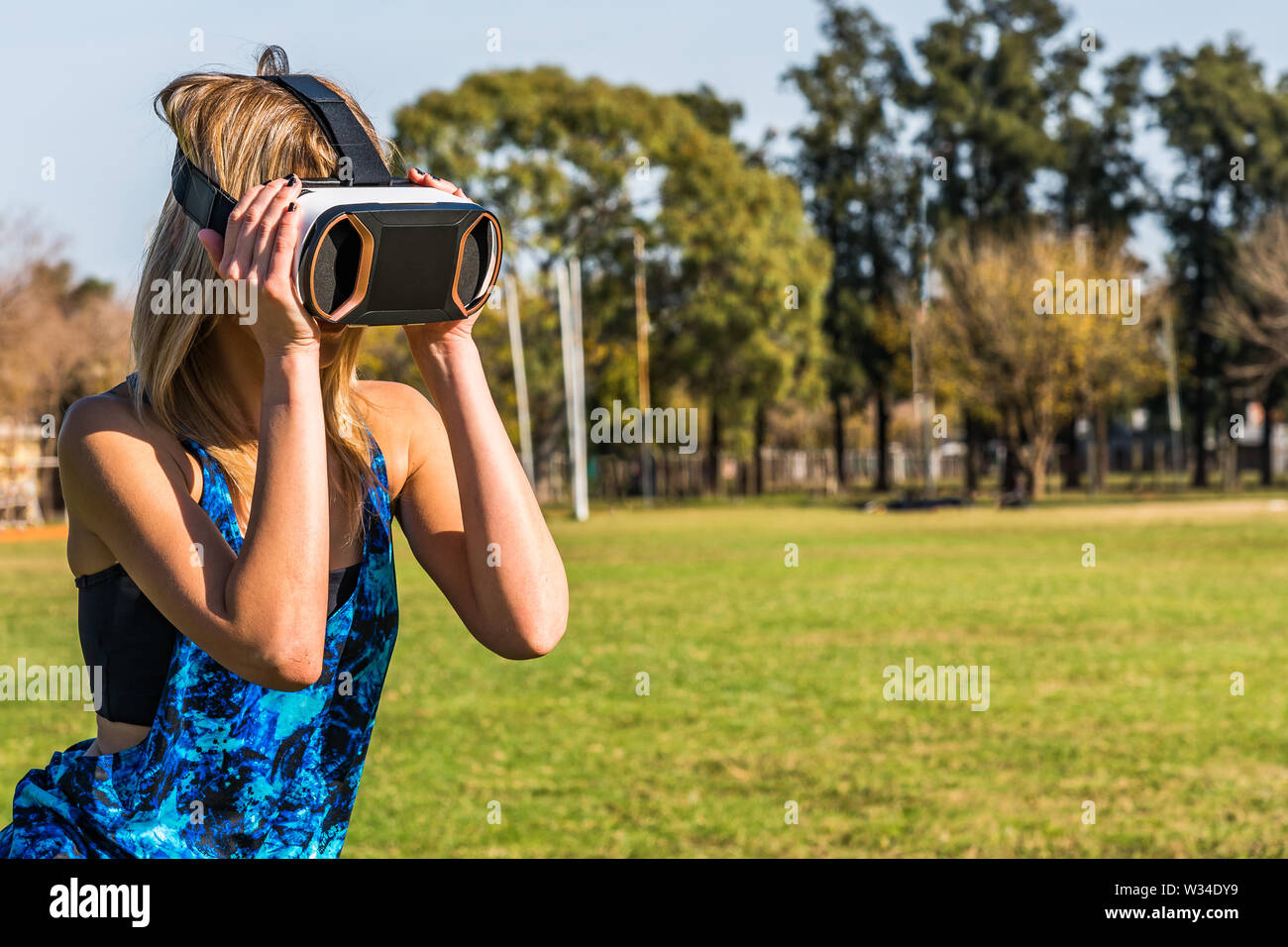 Kaukasische Frau im Park, blond mit virtueller Realität Maske an einem sonnigen Tag mit blauen Himmel Stockfoto