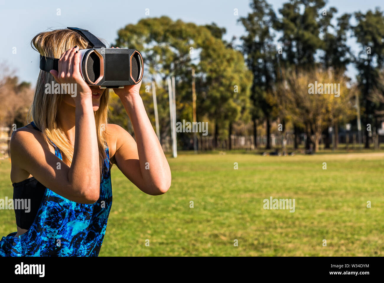 Kaukasische Frau im Park, blond mit virtueller Realität Maske an einem sonnigen Tag mit blauen Himmel Stockfoto