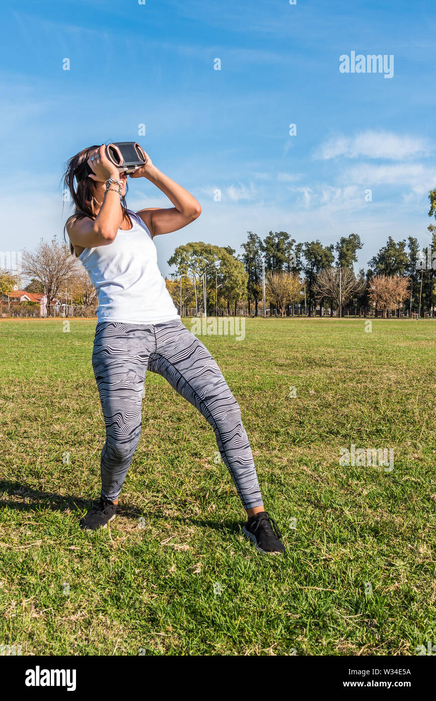 Kaukasische Frau im Park, brünett mit virtueller Realität Maske an einem sonnigen Tag mit blauen Himmel Stockfoto