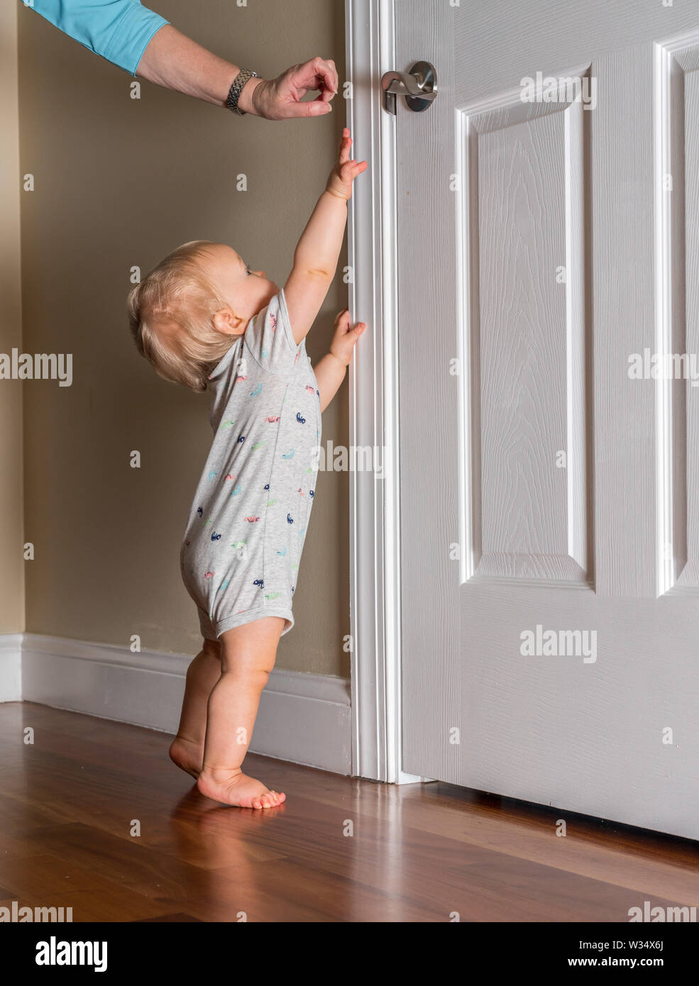 Junge Baby gerade laufen kann, bis die Tür auf Holzboden Griff Stockfoto