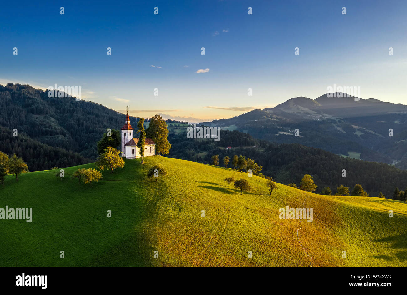 Skofja Loka, Slowenien - Luftbild der schönen Hügel Sveti Tomaž (Hl. Thomas) Kirche mit einem warmen Sommer Sonnenuntergang, klare blaue Himmel und Julian Al Stockfoto