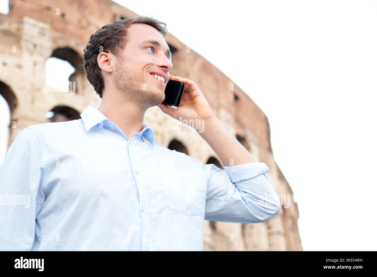Business Mann auf Handy, Kolosseum, Rom, Italien. Junge Unternehmer mit Smartphone außerhalb Glücklich lächelnde im casual Shirt vor dem Kolosseum. Kaukasier Männlich Professional in Europa. Stockfoto