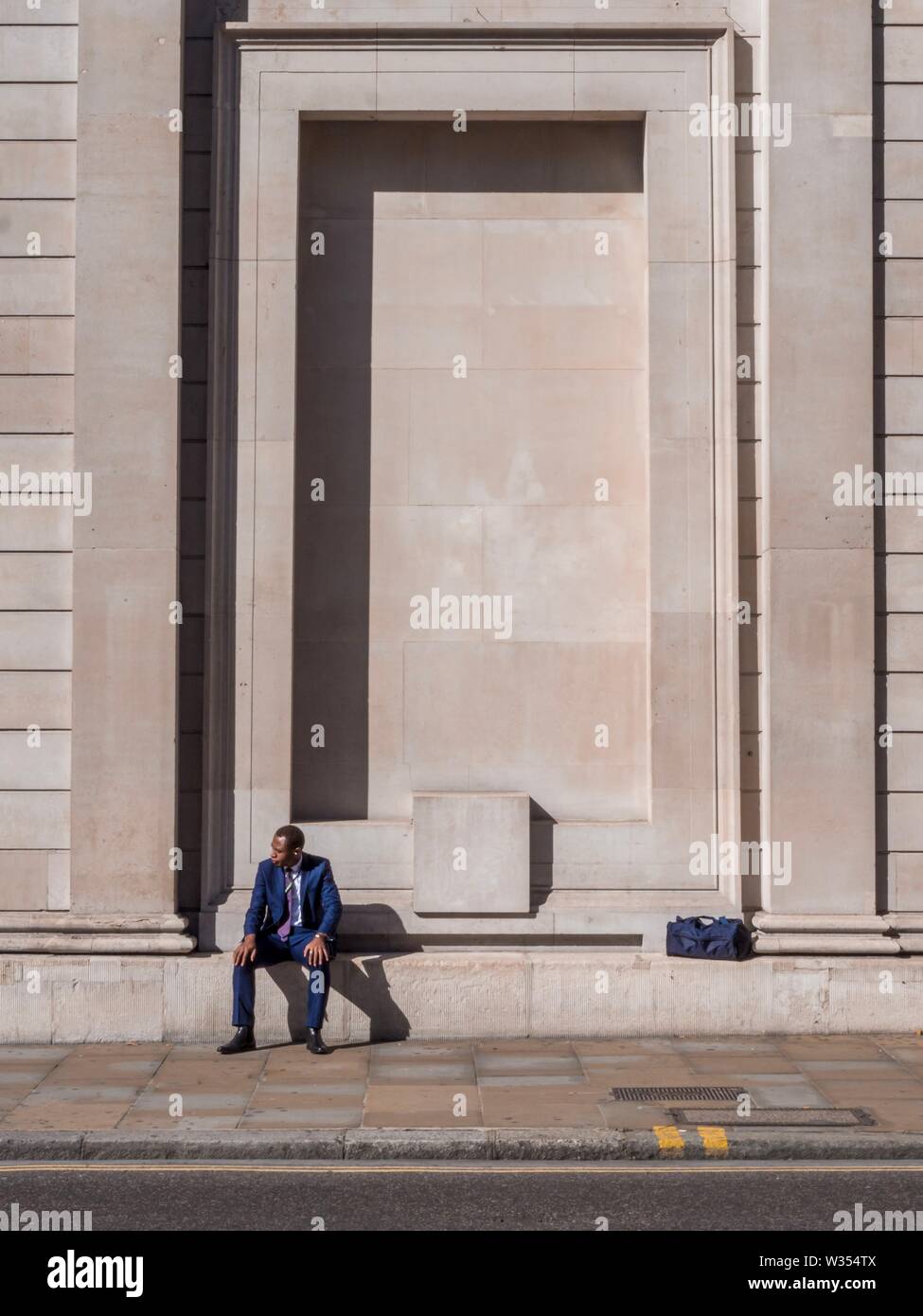 Ein Mann im Anzug auf einem Felsvorsprung ausserhalb der Bank von England sitzen Stockfoto
