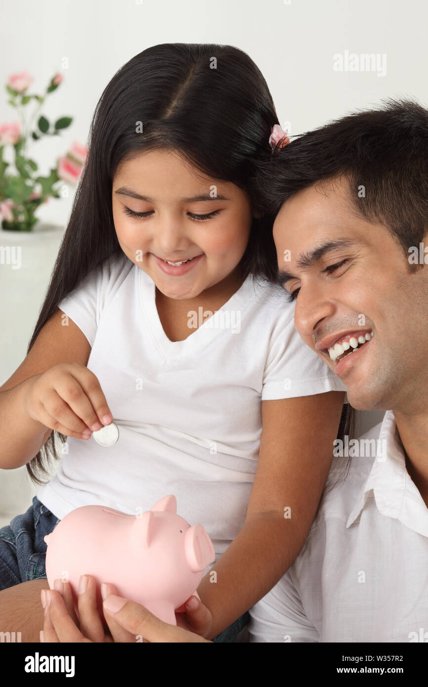 Indisches Mädchen, Münze in ein Sparschwein mit ihrem Vater. Stockfoto