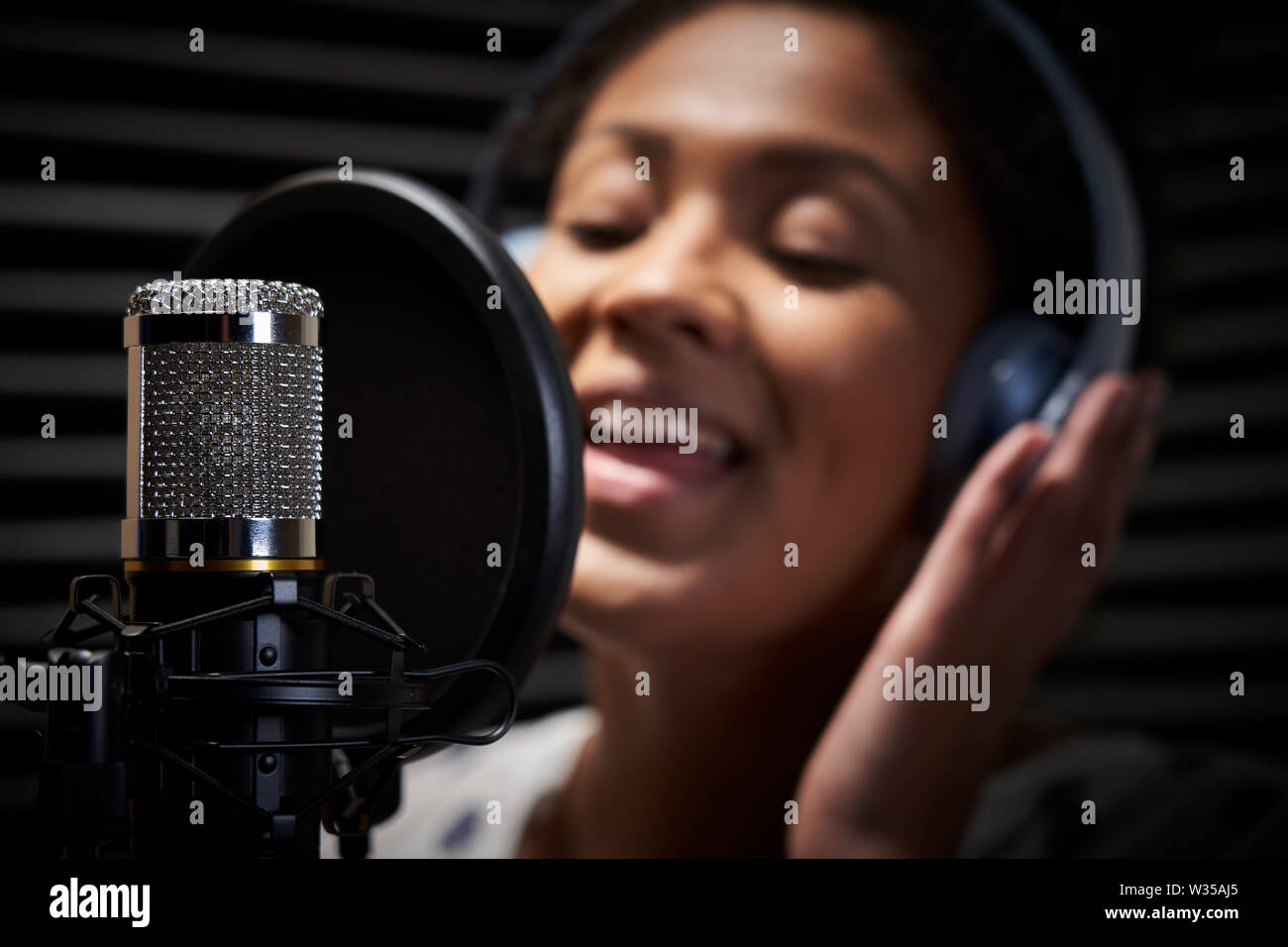 Sängerin mit Kopfhörern singen Sie in das Mikrofon in Studio Stockfoto