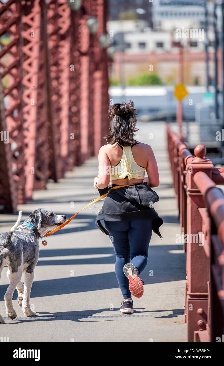 Das Mädchen in Sportkleidung macht ein Run auf die Brücke, um Gewicht zu verlieren und ihr Körper in einer attraktiven Form halten, und auch Ihr Hund an der Leine, die ru zu Fuß Stockfoto