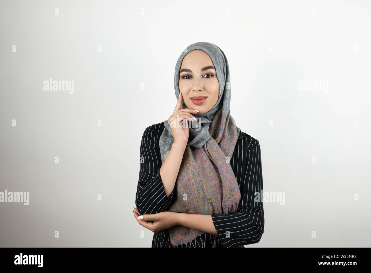Junge schöne Muslimischen business Frau mit Turban hijab Kopftuch berühren Ihr Gesicht mit einer Hand in stehender Position isoliert weißer Hintergrund Stockfoto