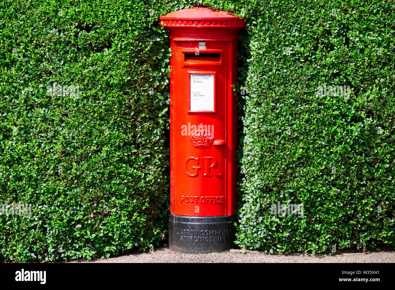 London, England/Großbritannien - 13. Juli 2019: Royal Mail rote Säule Postbox in Hecke Bush versteckt Stockfoto