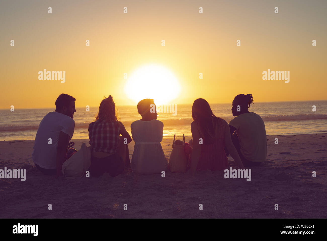 Freunde sitzen zusammen am Strand bei Sonnenuntergang Stockfoto