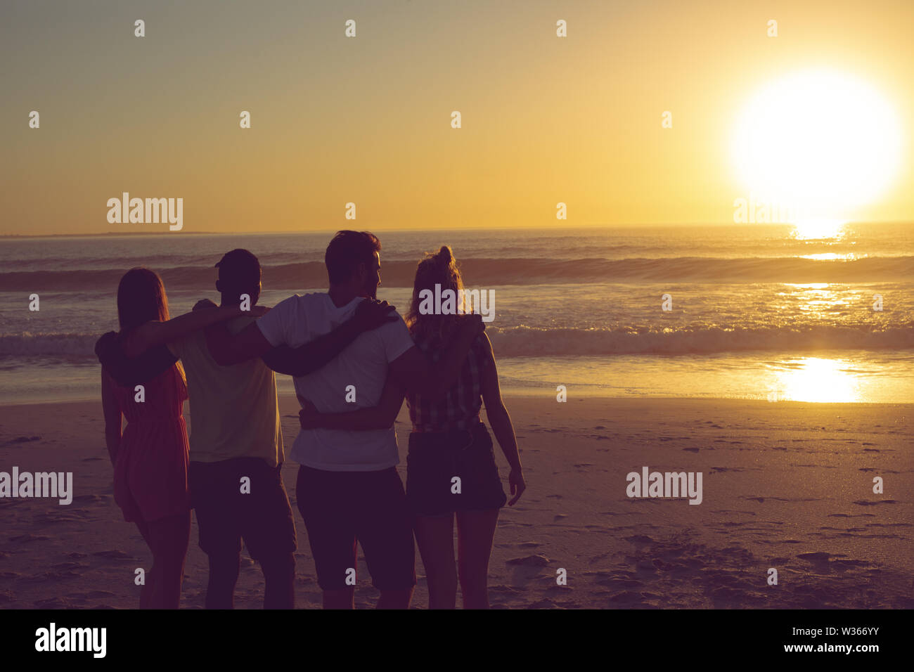 Freunde stehend mit Arme um am Strand bei Sonnenuntergang Stockfoto