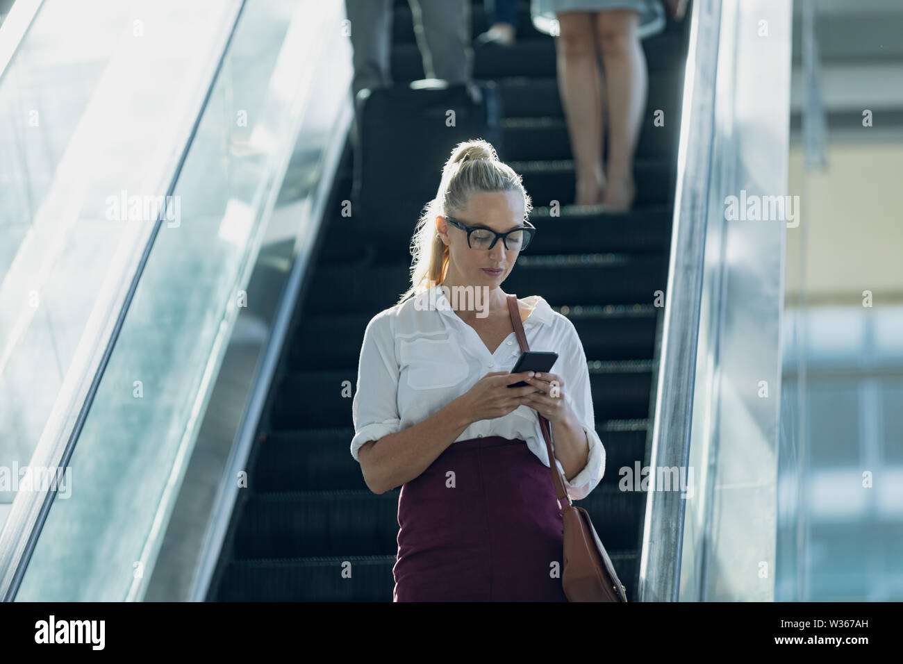 Kaukasische Geschäftsfrau auf Mobiltelefon während der Verwendung von Fahrtreppen in modernen Büro Stockfoto