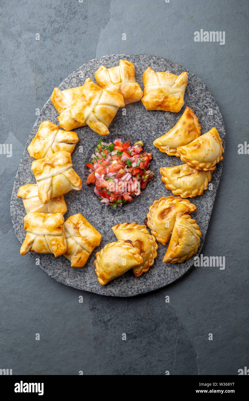 Verschiedene kleine Cocktail EMPANADAS auf der Steinplatte mit Tomatensauce und Guacamole. Grauer Hintergrund. Lateinamerikanische und Spanische typische Lebensmittel. Stockfoto