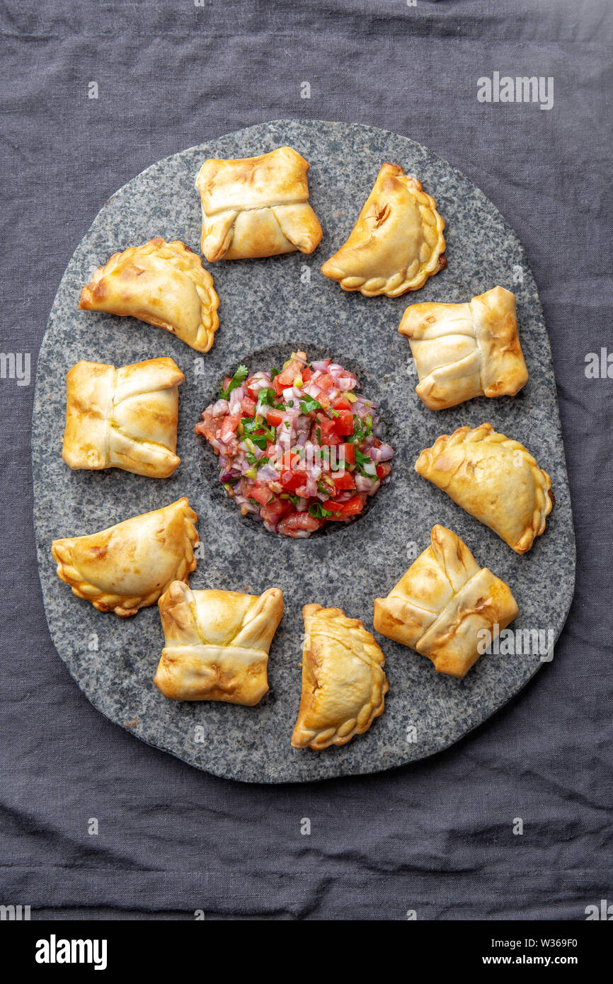 Verschiedene kleine Cocktail EMPANADAS auf der Steinplatte mit Tomatensauce und Guacamole. Grauer Hintergrund. Lateinamerikanische und Spanische typische Lebensmittel Stockfoto