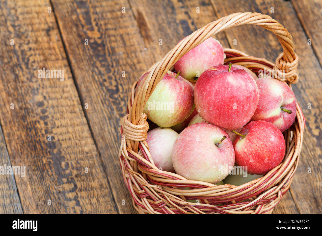 Reife äpfel mit Wassertropfen im Weidenkorb auf Holzplatten. Flache Tiefenschärfe, Ansicht von oben. Stockfoto