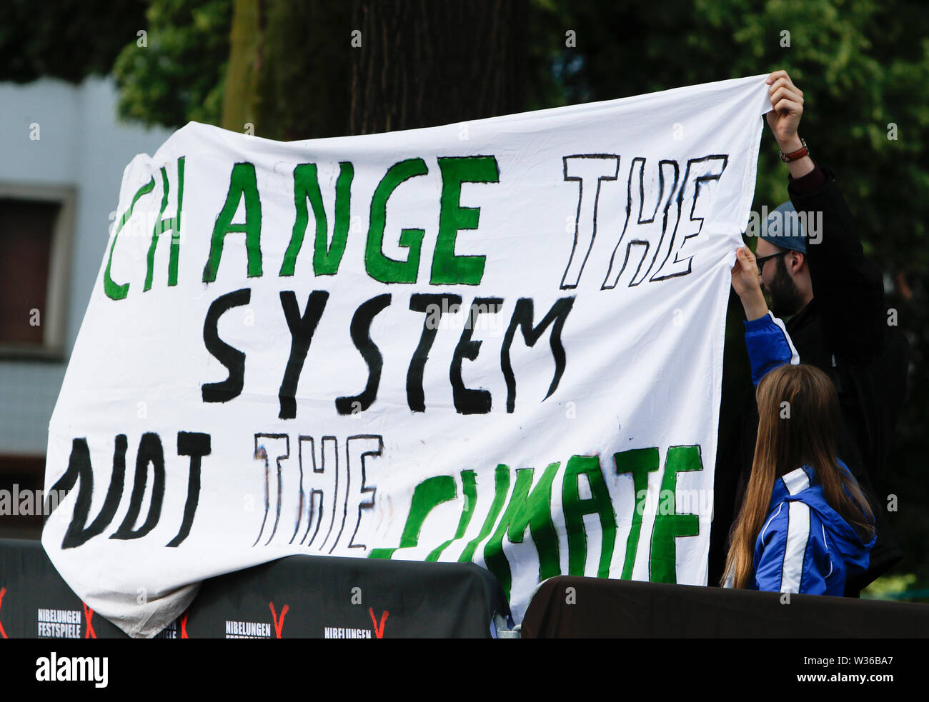 Worms, Deutschland. 12. Juli, 2019. Worms, Deutschland. 12. Juli, 2019. Demonstranten, die gegen den Klimawandel halten ein Banner mit der Aufschrift 'Ändern Sie das System, nicht das Klima". Schauspieler, Politiker und andere VIPs nahmen an der Eröffnung der Nibelungen-festspiele Nibelungen-Festspiele (2019) in Worms. Das Spiel in der 18. Saison des Festivals ist "Uberwaltigung' (Überwinden) zum Thema Thomas Melle, und von Lilja Rupprecht geleitet. Es erzählt von der ursprünglichen Lied der Nibelungen, beginnend am Ende und versucht, die Geschichte zu einem besseren, weniger tödlichen Versuch umschreiben. Credit: PACIFIC PRESS/Alamy Stockfoto