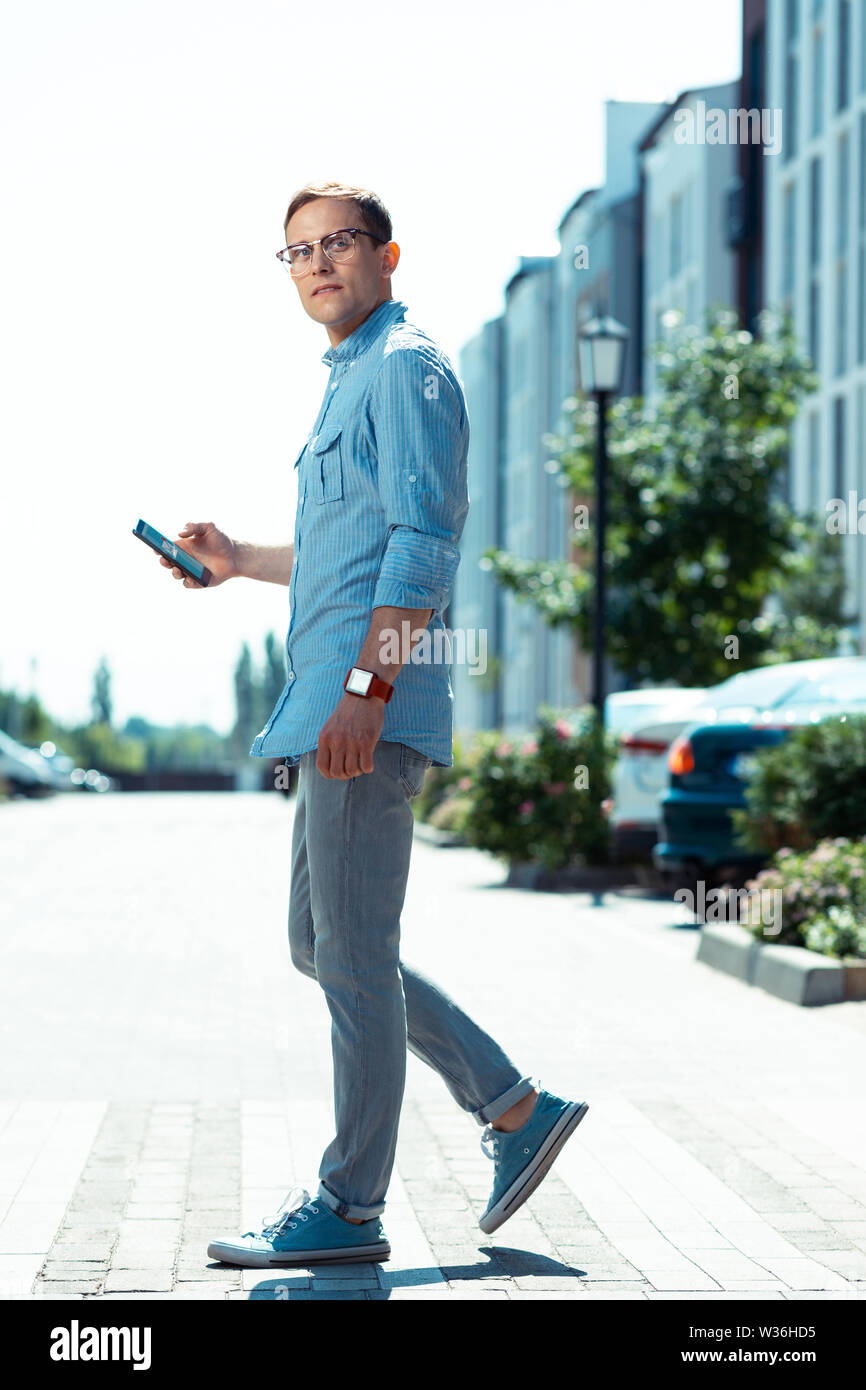 Stilvolle dunkelhaarigen Mann in Gläsern holding Telefon beim Gehen Stockfoto