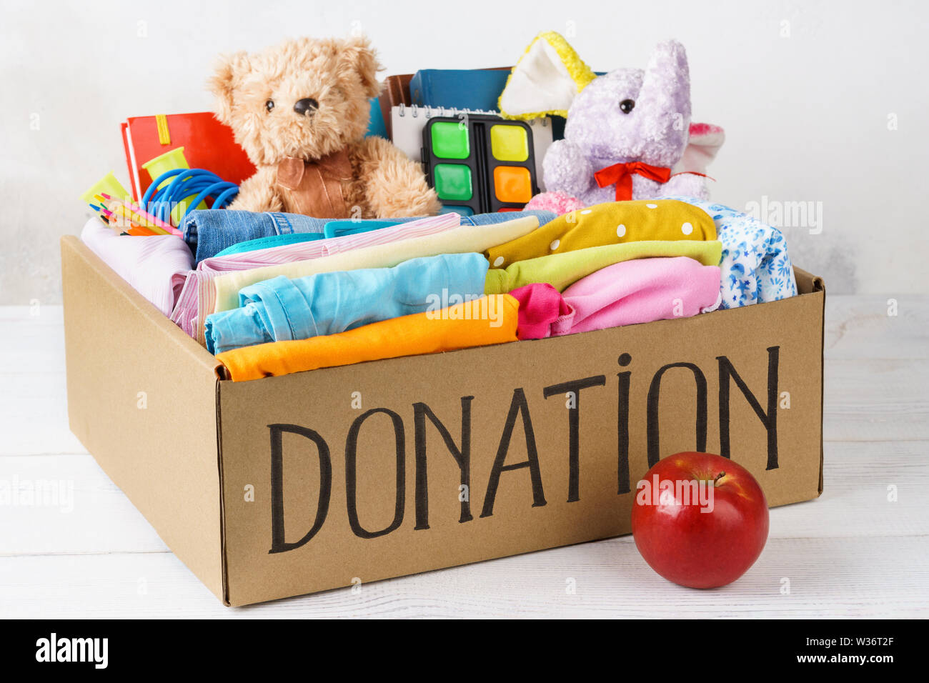 Verschiedene Spenden in einer Box - Kleidung, Schreibwaren und Spielwaren. Kleidung für Kinder und Jugendliche. Vorbereitung für die Schule. Stockfoto