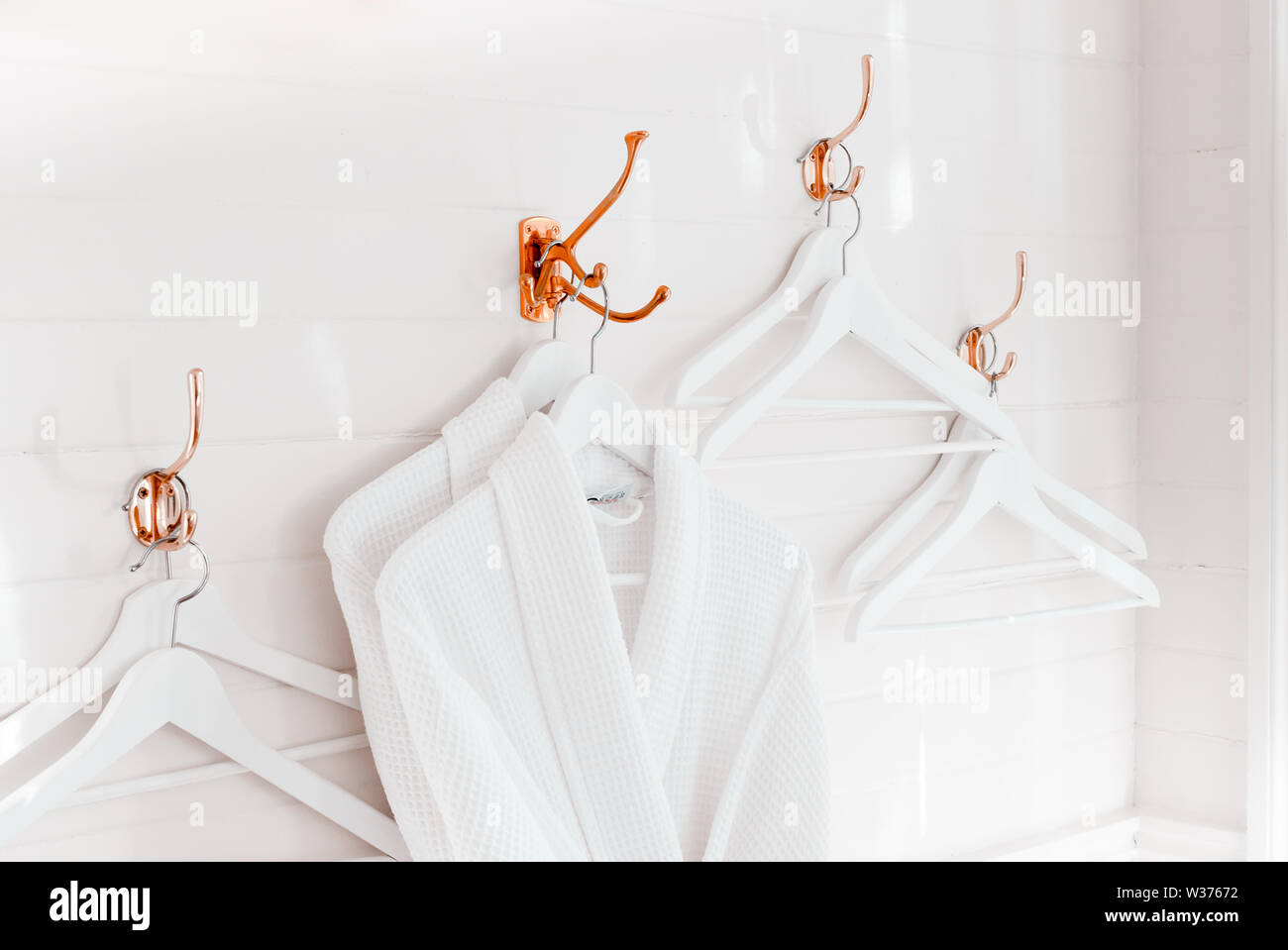 Zwei weiße Baumwolle hingen Bademäntel von Rose Gold Haken an der weißen Wand mit anderen leere Kleiderbügel Stockfoto