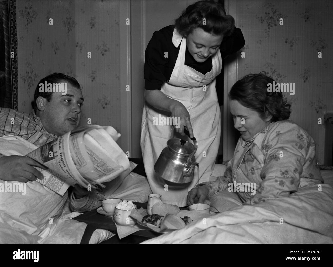 Leben in den 1940er Jahren. Eine junge Frau, die als Dienstmädchen serviert morgens Kaffee zu Herrn und Frau, während sie noch im Bett sind. Sie ist ordentlich in einem weißen Schürze gekleidet. Schweden 1940. Kristoffersson ref 55-8 Stockfoto
