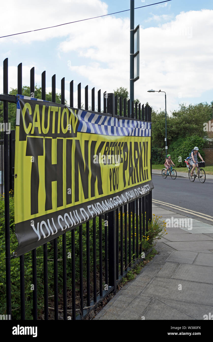 Erwachsene und Kinder Zyklus durchlaufen, bevor sie Park, Zeichen an Fahrer außerhalb einer Schule in Twickenham, Middlesex, England ein Denken Stockfoto