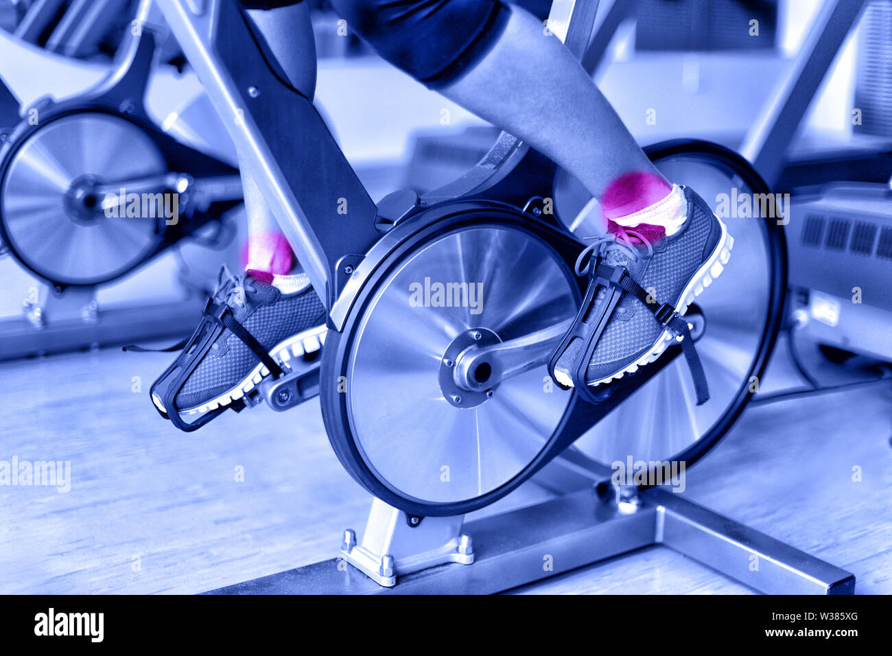 Sportverletzung - Knöchel Schmerz während der Ausbildung auf dem spinningbike im Fitnessstudio. Nahaufnahme der Beine der weiblichen Athleten mit Fahrrad Maschine im Fitnesscenter in Blau monochromatischen Filter. Stockfoto
