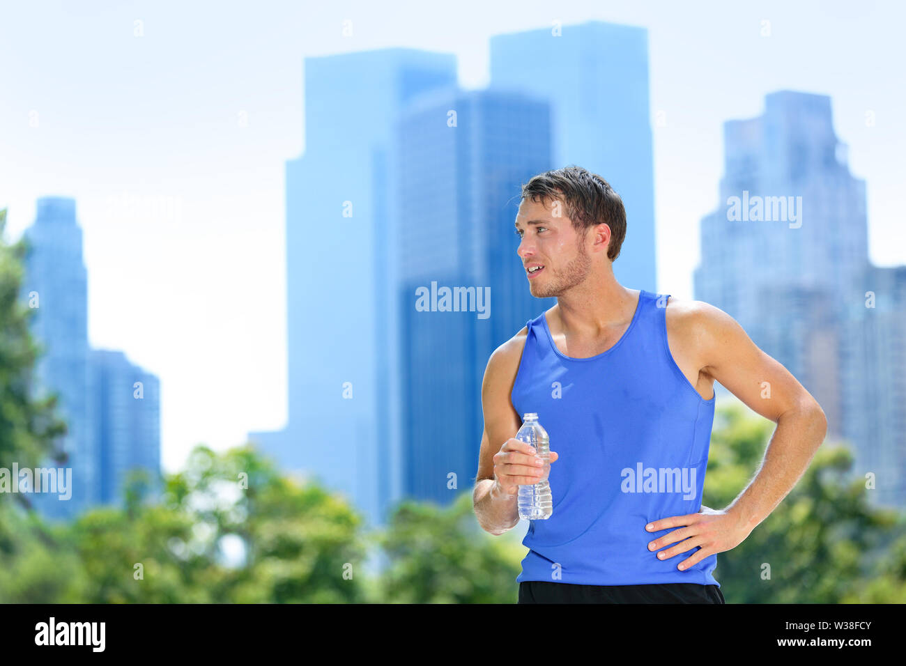 Sport mann Trinkwasser Flasche in New York City. Männliche Läufer verschwitzt und durstig nach im Central Park, New York City, Manhattan, mit der städtischen Gebäude Skyline im Hintergrund. Stockfoto