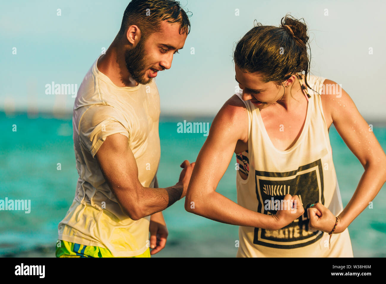 Junge fröhliche weibliche und männliche Schwimmer s flexing Biceps gegen blaue Meer Stockfoto