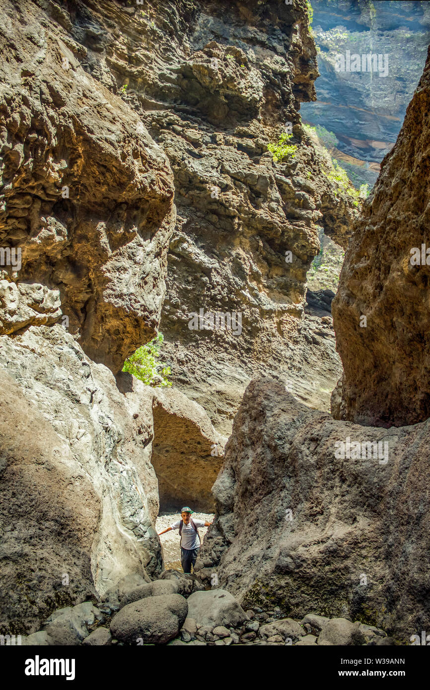 Junge Reisende bleibt an der Spitze der riesigen Felsbrocken in die Masca Schlucht, Teneriffa, mit erstarrter Lava Flow Schichten und arch Bildung. Schlucht Stockfoto