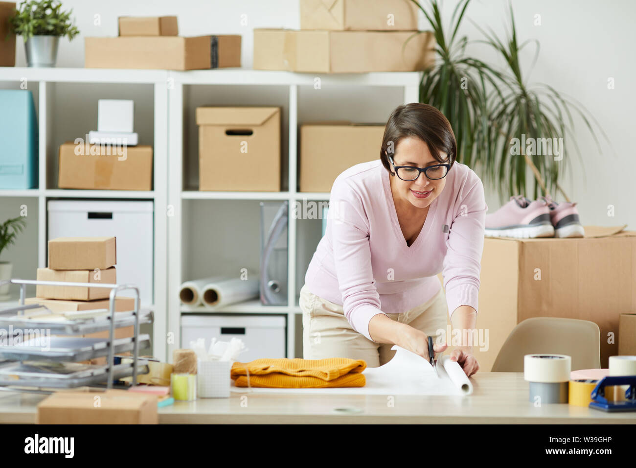 Junge Manager in casualwear Biegen über Schreibtisch und das Schneiden von Papier vor der Verpackung gelb Pullover Stockfoto