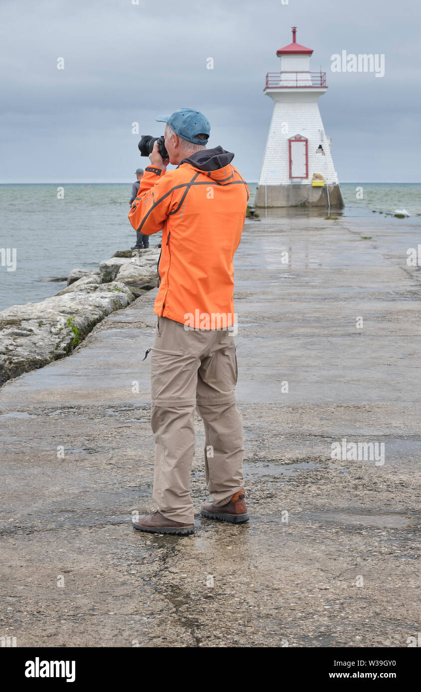 Fotograf tragen leuchtend orange Jacke nimmt Bilder auf einem kühlen trüben und regnerischen Morgen in der Nähe von einem Leuchtturm. Stockfoto