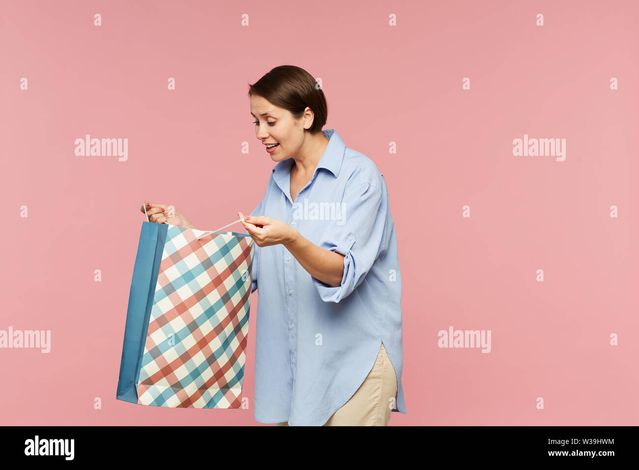 Junge aufgeregt weiblich in casualwear auf Überraschung in offenen paperbag Während posieren in Isolation Stockfoto