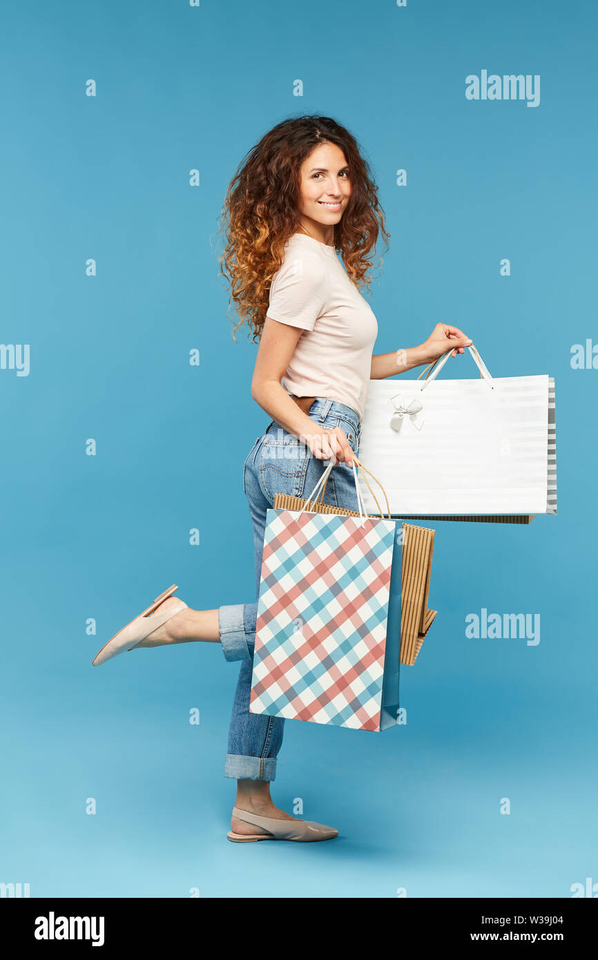 Hübsche junge Shopper in casualwear Holding paperbags beim Stehen in der Studio der blauen Wand Stockfoto