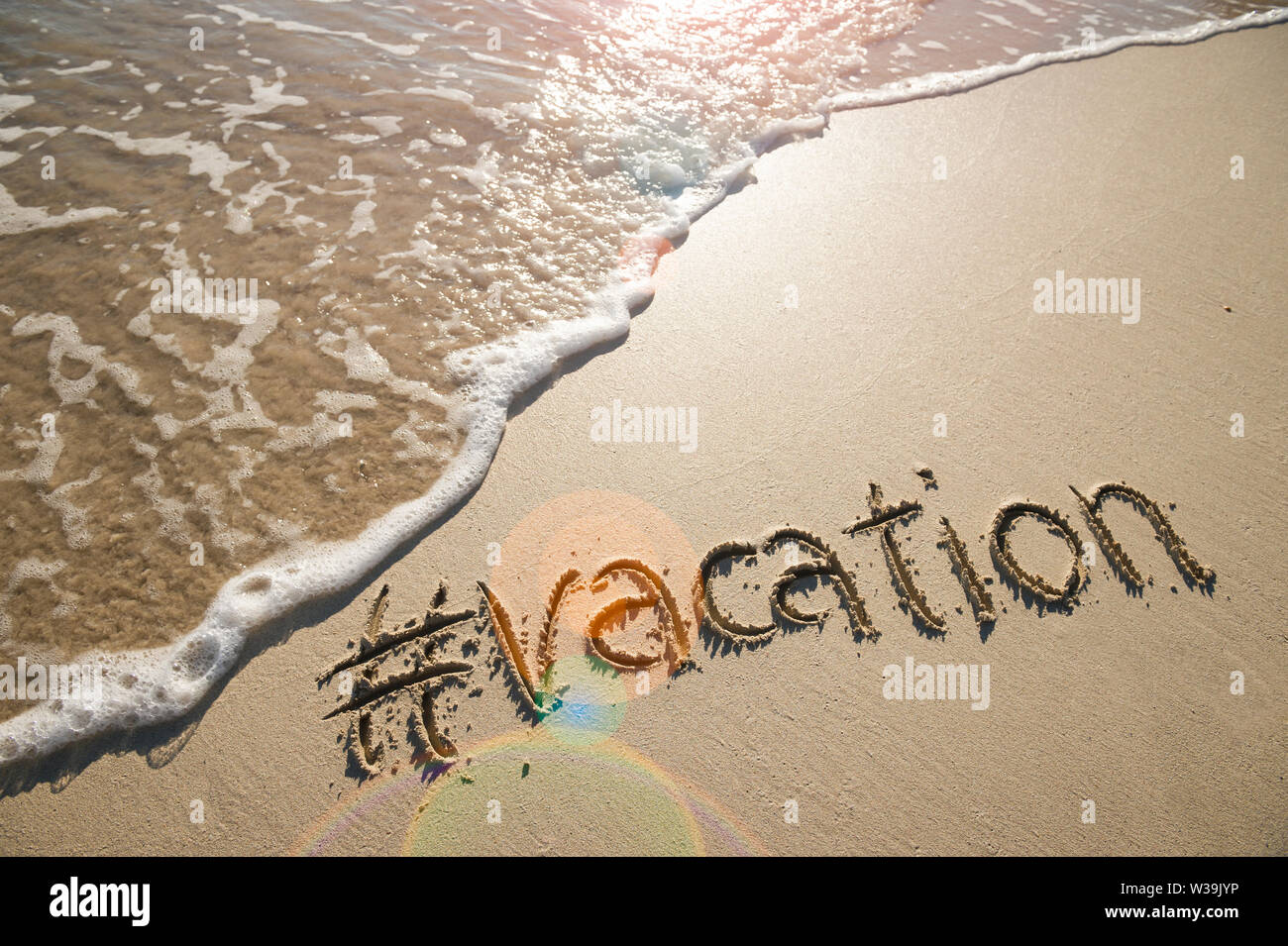 Modernes reisen Nachricht für den Strand mit einem Social Media - freundliche Hashtag mit dem Wort "Urlaub" in Glatten Sand mit ankommenden Welle geschrieben Stockfoto