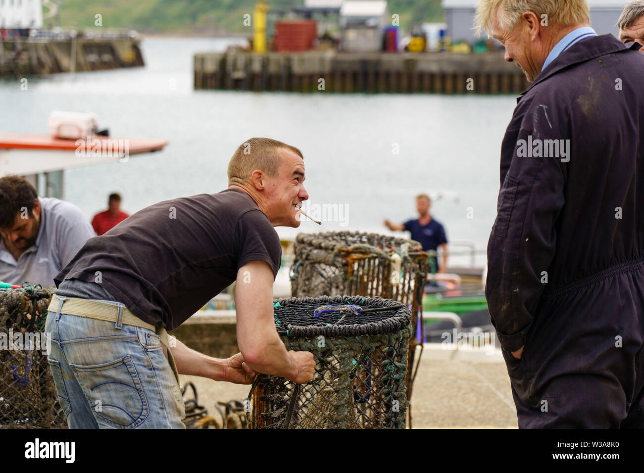 Fischer rauchen eine Zigarette, während sie Hummer-Töpfe an einer Hafenpromenade in Scarborough, North Yorkshire, England, Großbritannien reparieren. Stockfoto