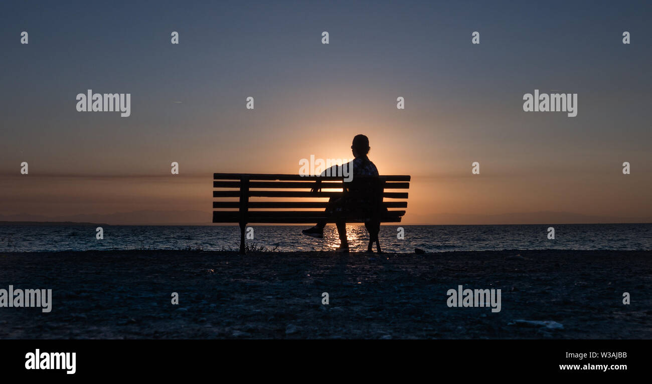 Silhoutte sitzt auf der Bank bei Sonnenuntergang auf der Suche Stockfoto