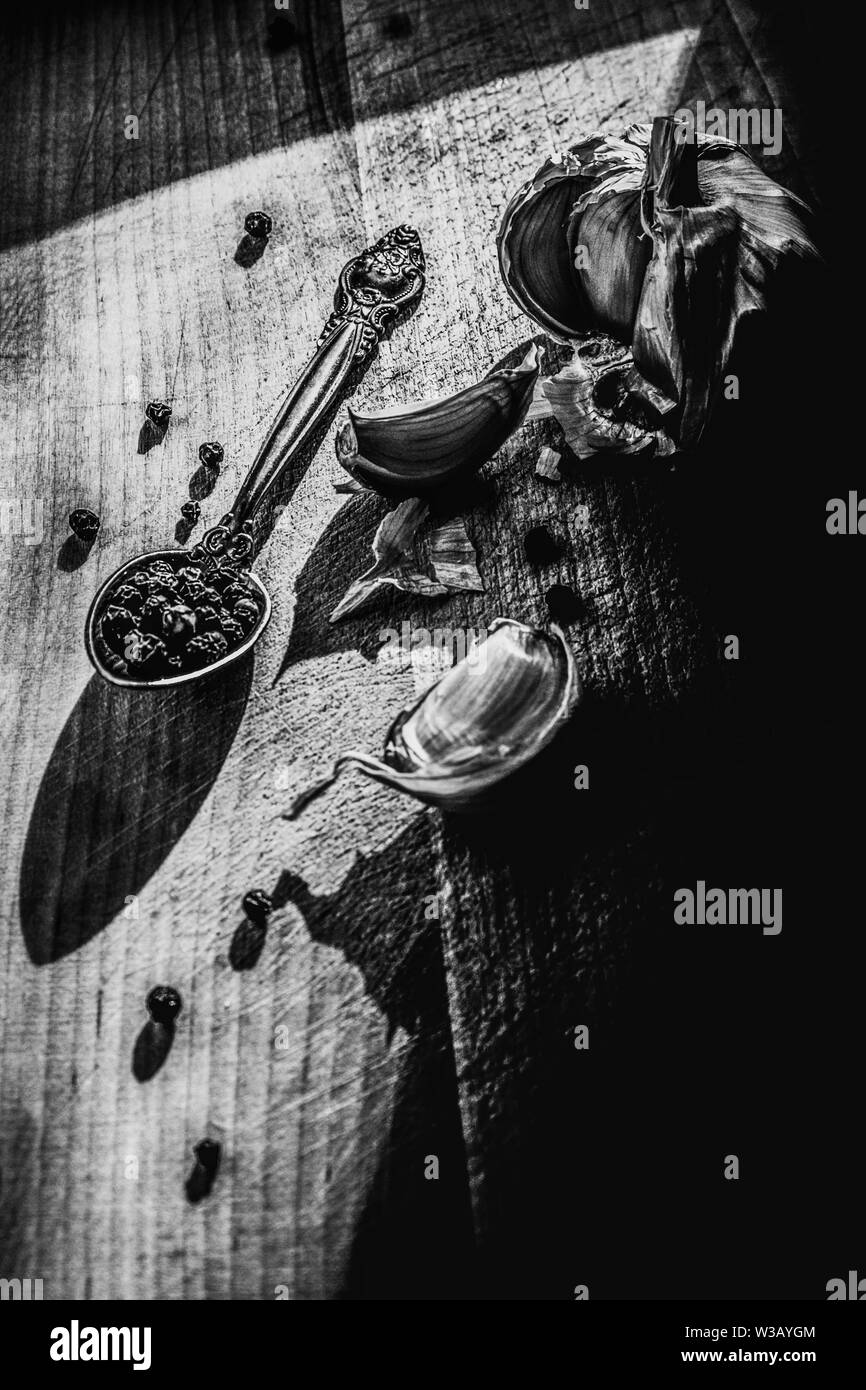 Immer noch leben. Knoblauch und Pfeffer schwarz Erbsen auf einem Holzbrett. Die Schwarz-Weiß-Fotografie. Stockfoto