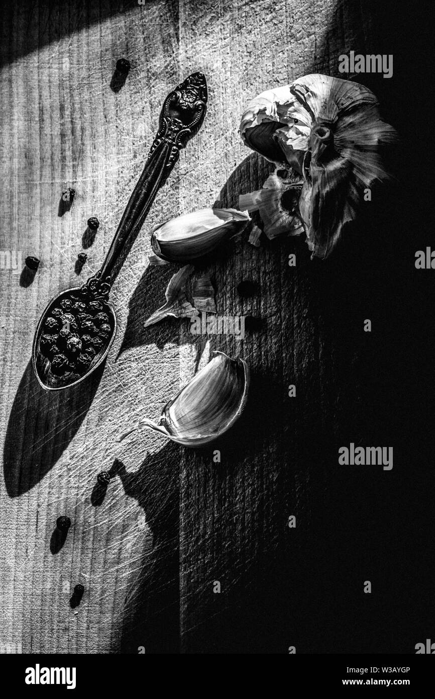 Immer noch leben. Knoblauch und Pfeffer schwarz Erbsen auf einem Holzbrett. Die Schwarz-Weiß-Fotografie. Stockfoto
