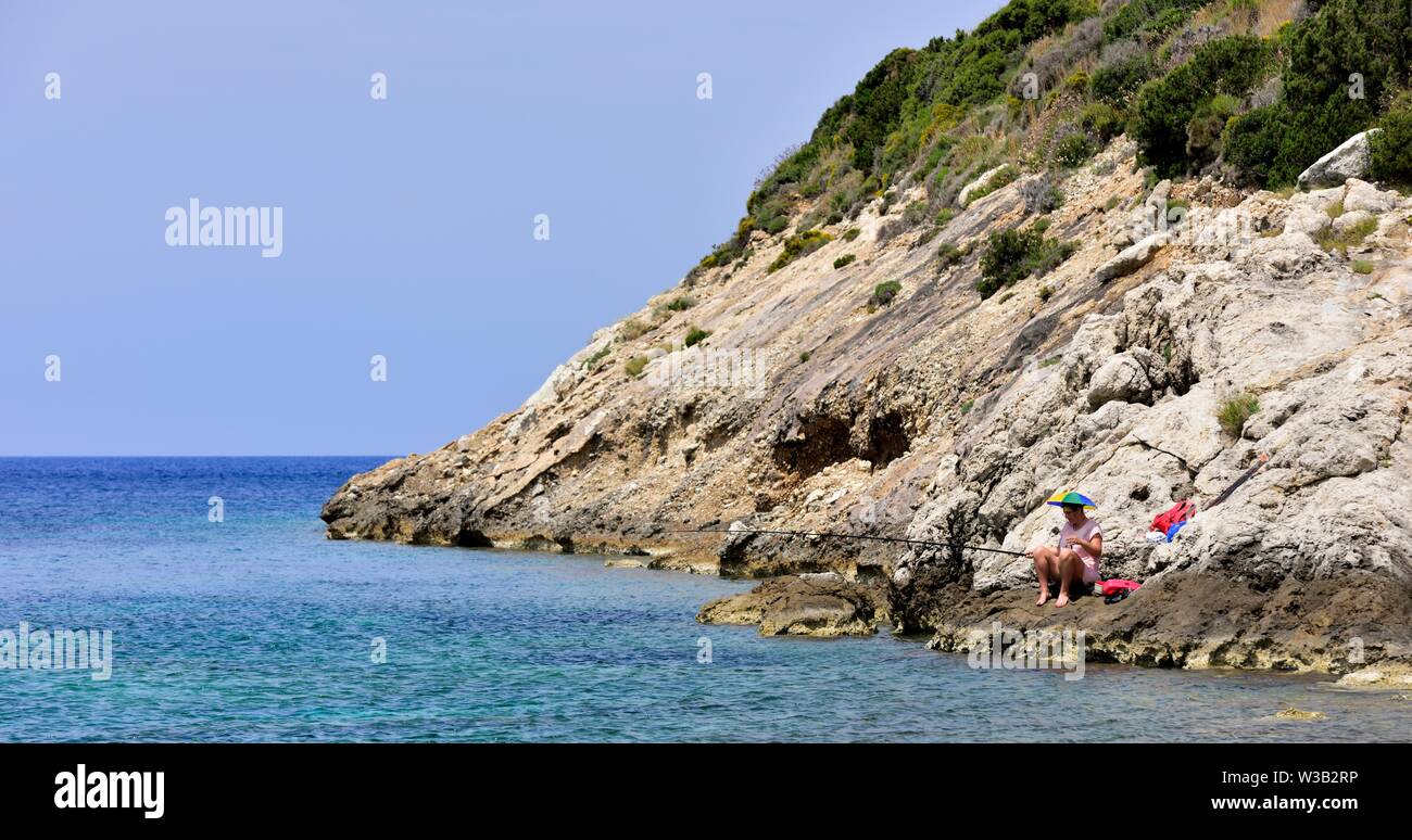 Eine Frau sitzt auf ein paar Felsen Meer angeln, Porto Timoni, Korfu, Griechenland Stockfoto