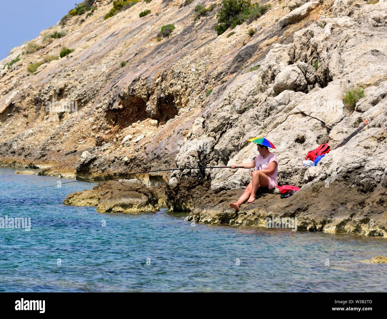 Eine Frau sitzt auf ein paar Felsen Meer angeln, Porto Timoni, Korfu, Griechenland Stockfoto