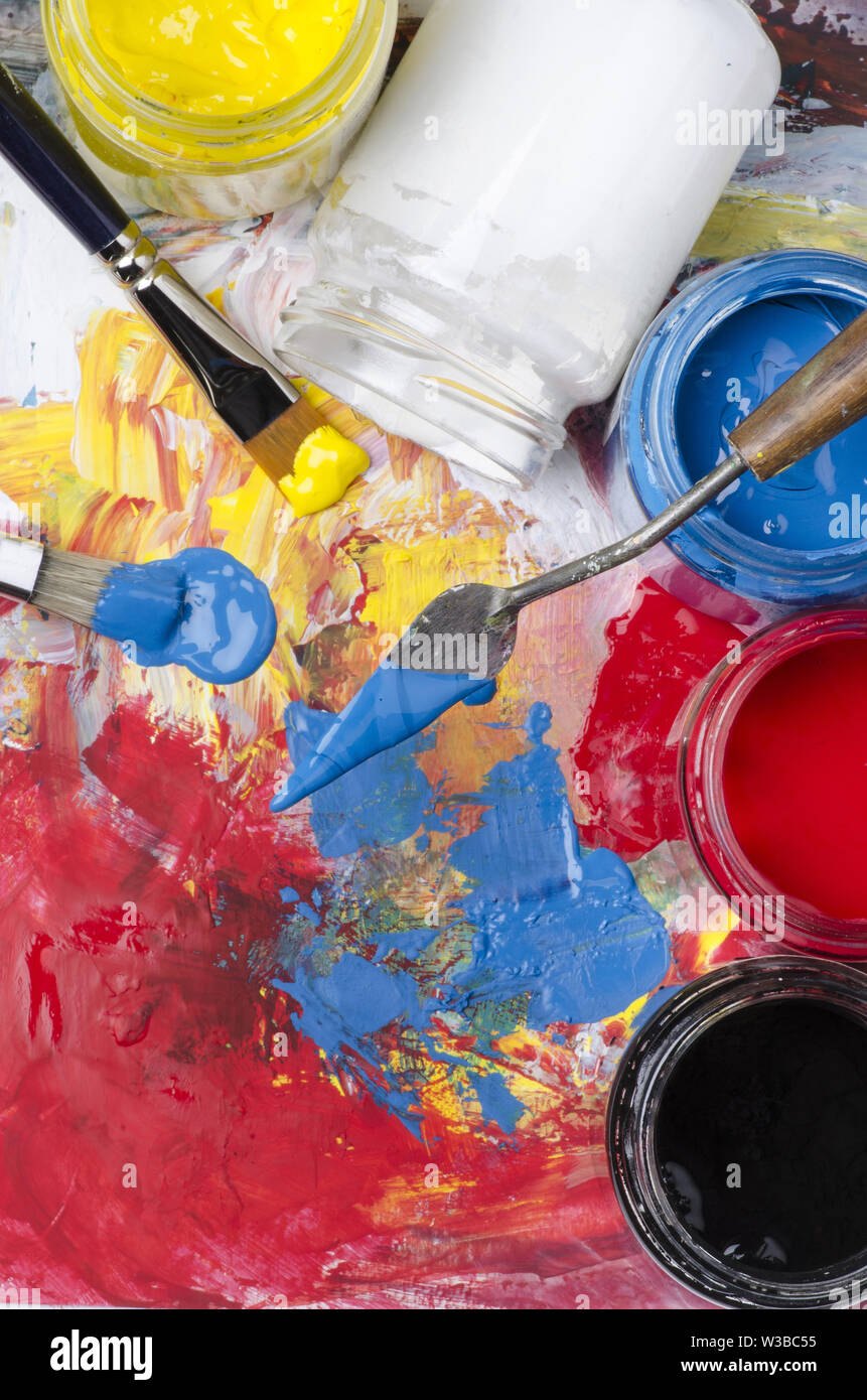 Gläser mit Acryl Farben und eine schmutzige Palette mit einem Spachtel und Pinsel Stockfoto