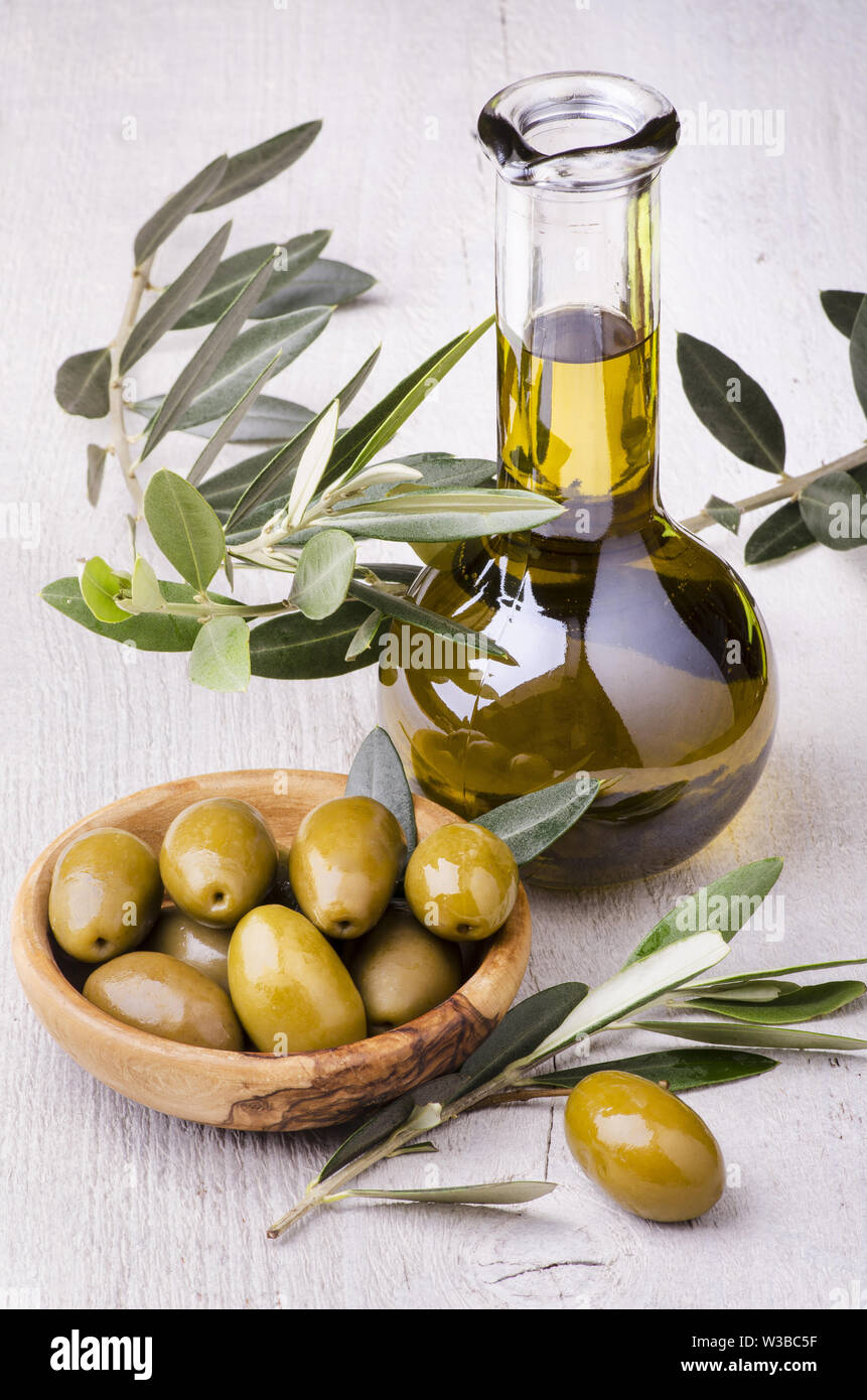 Olivenholz Schüssel mit riesigen grüne Oliven, Olive Branch, und Flasche mit extra natives Olivenöl Stockfoto