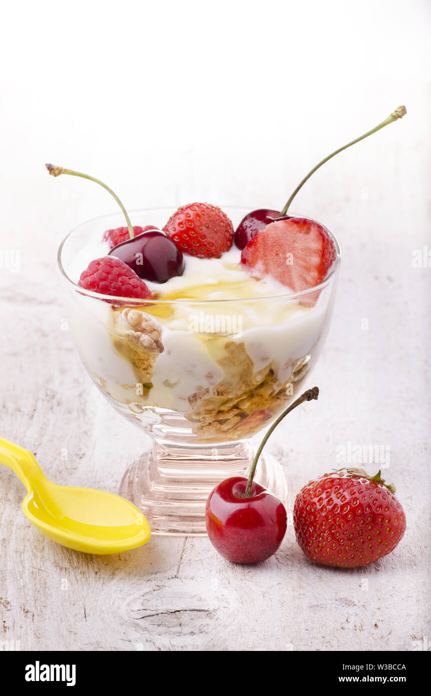 Exquisite Tasse mit frischem Joghurt, Honig und Obst mit Kirschen, Erdbeeren und Himbeeren Stockfoto