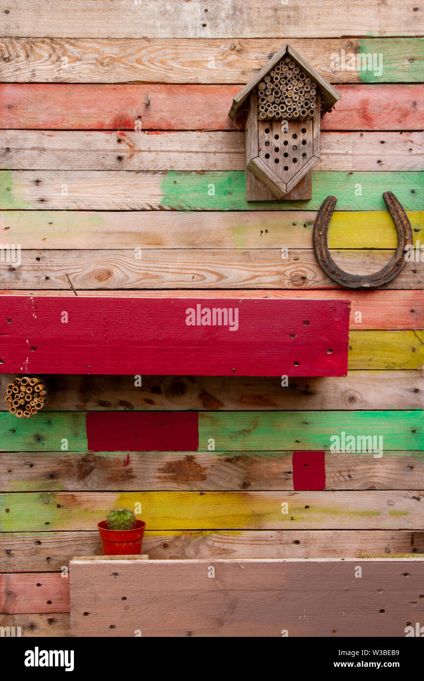Mehrfarbige Holztäfelung aus alten Paletten, mit einer Pflanzenbox, Lucky  Hufeisen und Insektenhotel, geeignet als Hintergrundbild Stockfotografie -  Alamy